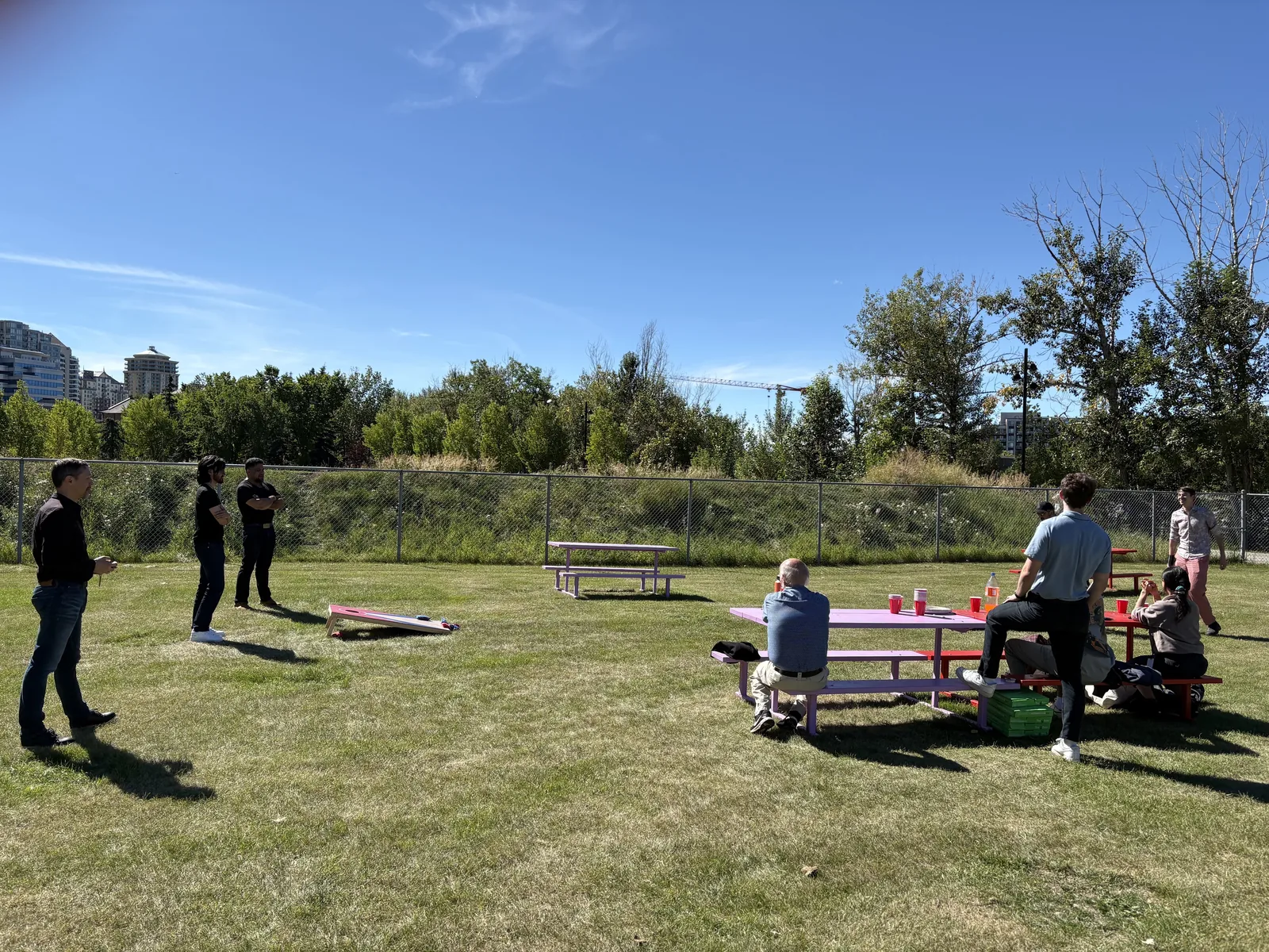 The Vencer team playing cornhole on a sunny field in Calgary, with picnic tables and the downtown skyline behind.