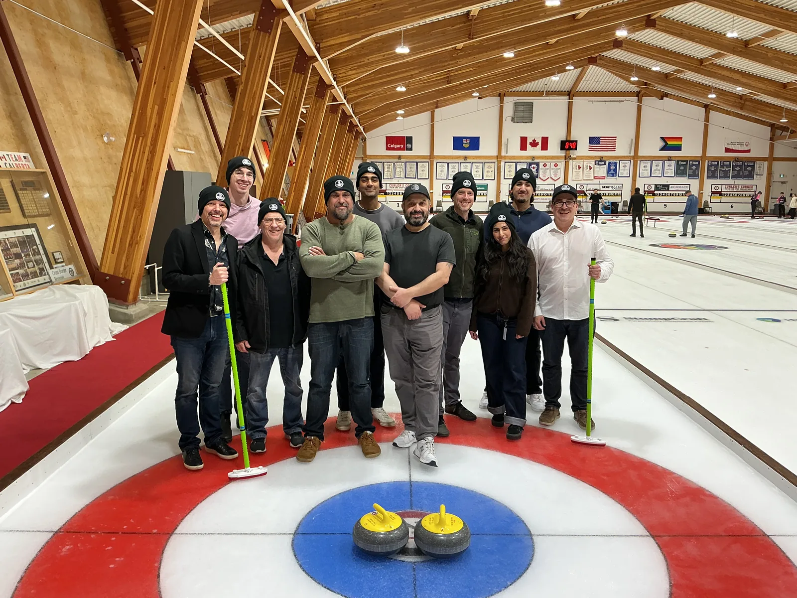 The Vencer team in matching toques on the ice at a Calgary curling club, brooms in hand, two stones on the button.